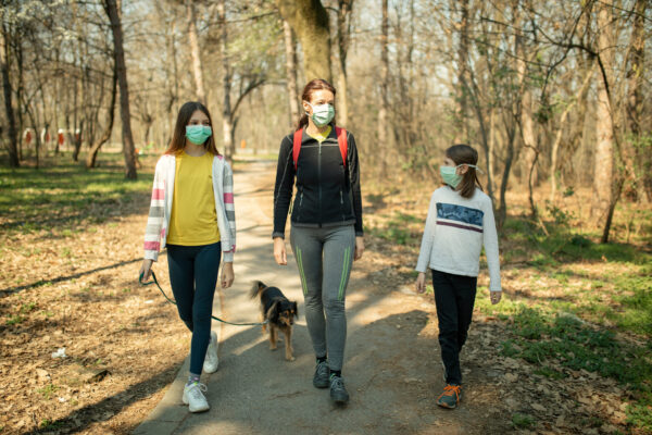 A mother with two children, walking their dog on a trail, wearing masks.