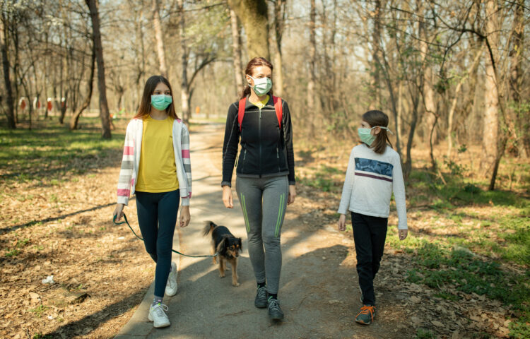 A mother with two children, walking their dog on a trail, wearing masks.