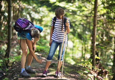 Mother and daughter hiking in forest. Mother is applying tick repellent on the daughter's legs.