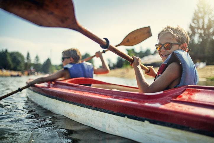 Two boys enjoying kayaking on lake on sunny summer day with life vests on demonstrating proper water safety