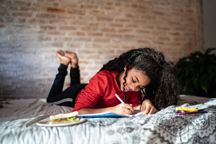 Girl writing on note pad or dairy lying on bed at home