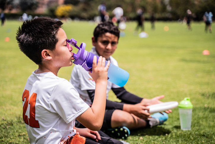 Boy drinking water at the public park to prevent dehydration in heat and summer