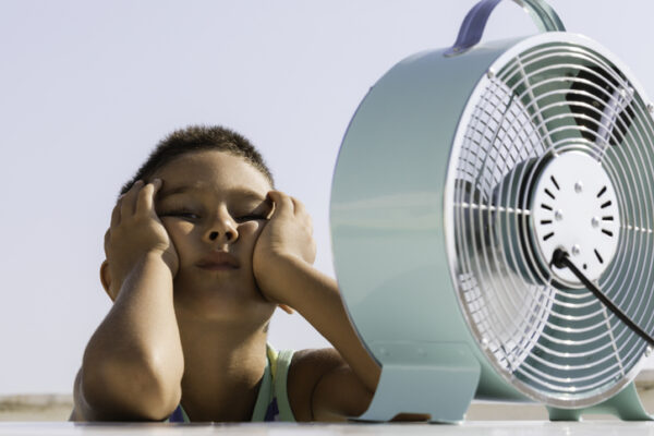 Overheated little child is sitting in front of electric fan trying to cool down.