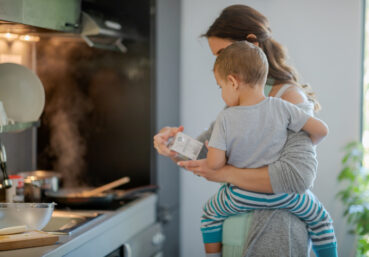 Mother with toddler on hip holding a carton of cooking cream and checking label