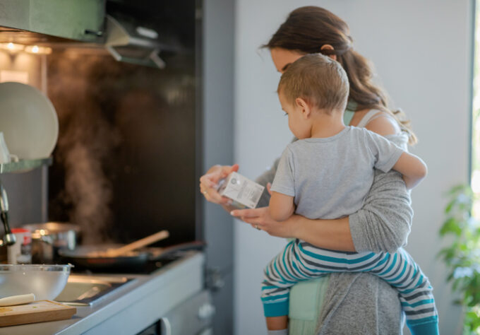 Mother with toddler on hip holding a carton of cooking cream and checking label