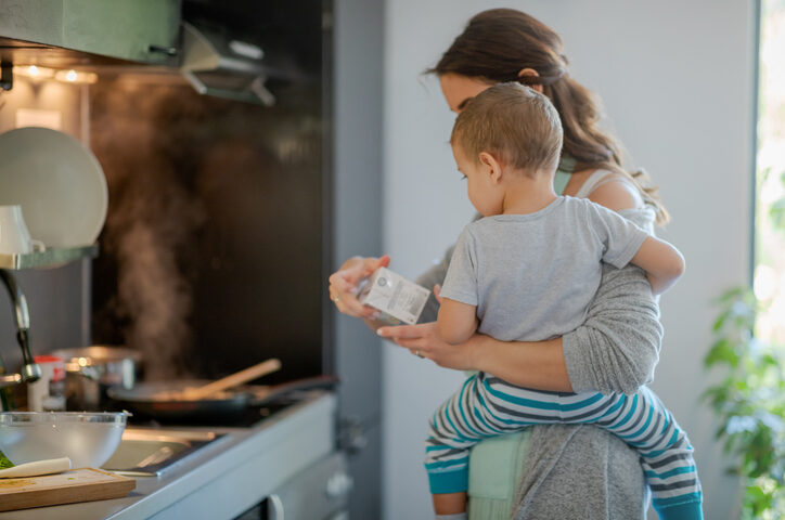 Mother with toddler on hip holding a carton of cooking cream and checking label