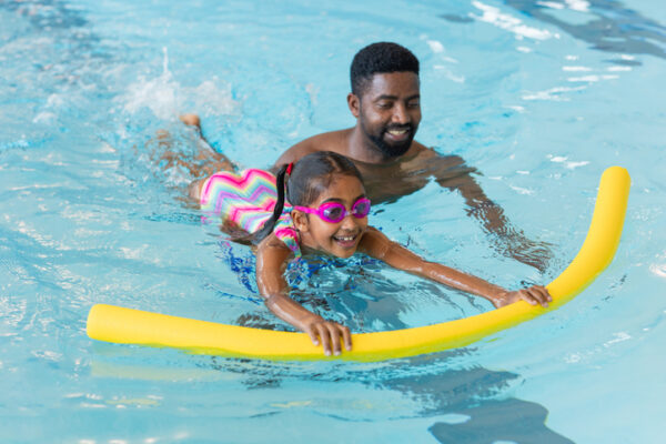 Father swimming with daughter using a noodle floatation device showing water safety