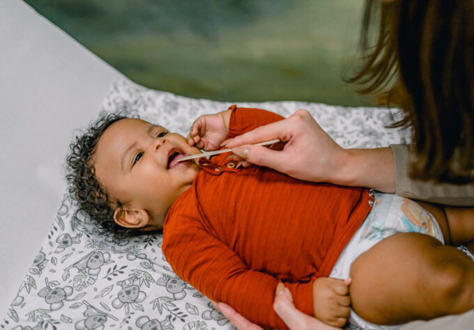 Pediatric ENT examining the mouth of a baby using a medical spatula in doctor's office to check for lip tie or tongue tie