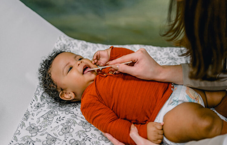 Pediatric ENT examining the mouth of a baby using a medical spatula in doctor's office to check for lip tie or tongue tie