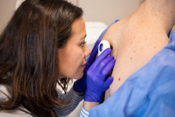 Female dermatologist examining her teen patient with a dermatoscope