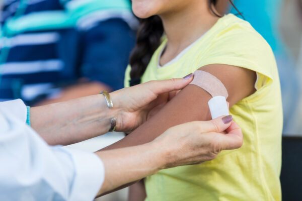 Doctor applies an adhesive bandage to preteen girl's arm after the girl receives a flu shot at an outdoor free clinic.