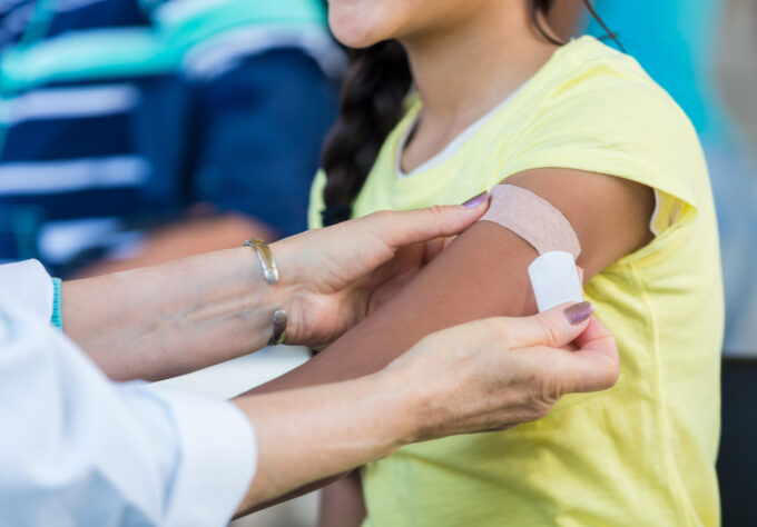 Doctor applies an adhesive bandage to preteen girl's arm after the girl receives a flu shot at an outdoor free clinic.