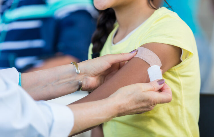 Doctor applies an adhesive bandage to preteen girl's arm after the girl receives a flu shot at an outdoor free clinic.