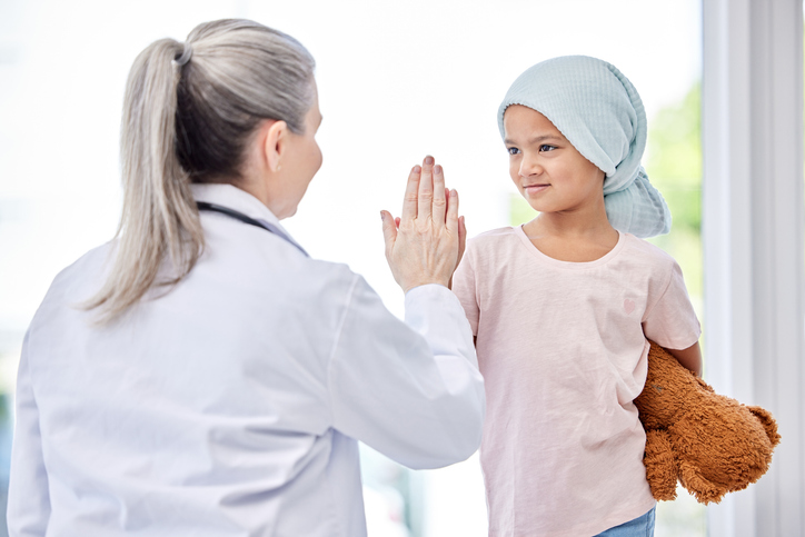 Shot of a little girl giving a doctor a high five in a clinic symbolizing the importance of partnership in pediatric cancer care and support