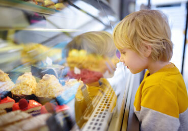 Little boy with food allergies is admiring cakes and other sweets on the showcase in cafe or supermarket.