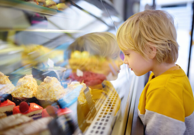 Little boy with food allergies is admiring cakes and other sweets on the showcase in cafe or supermarket.