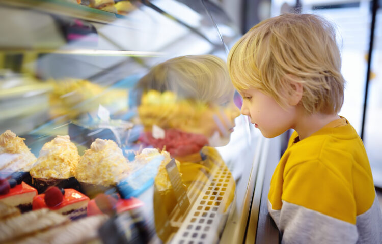 Little boy with food allergies is admiring cakes and other sweets on the showcase in cafe or supermarket.