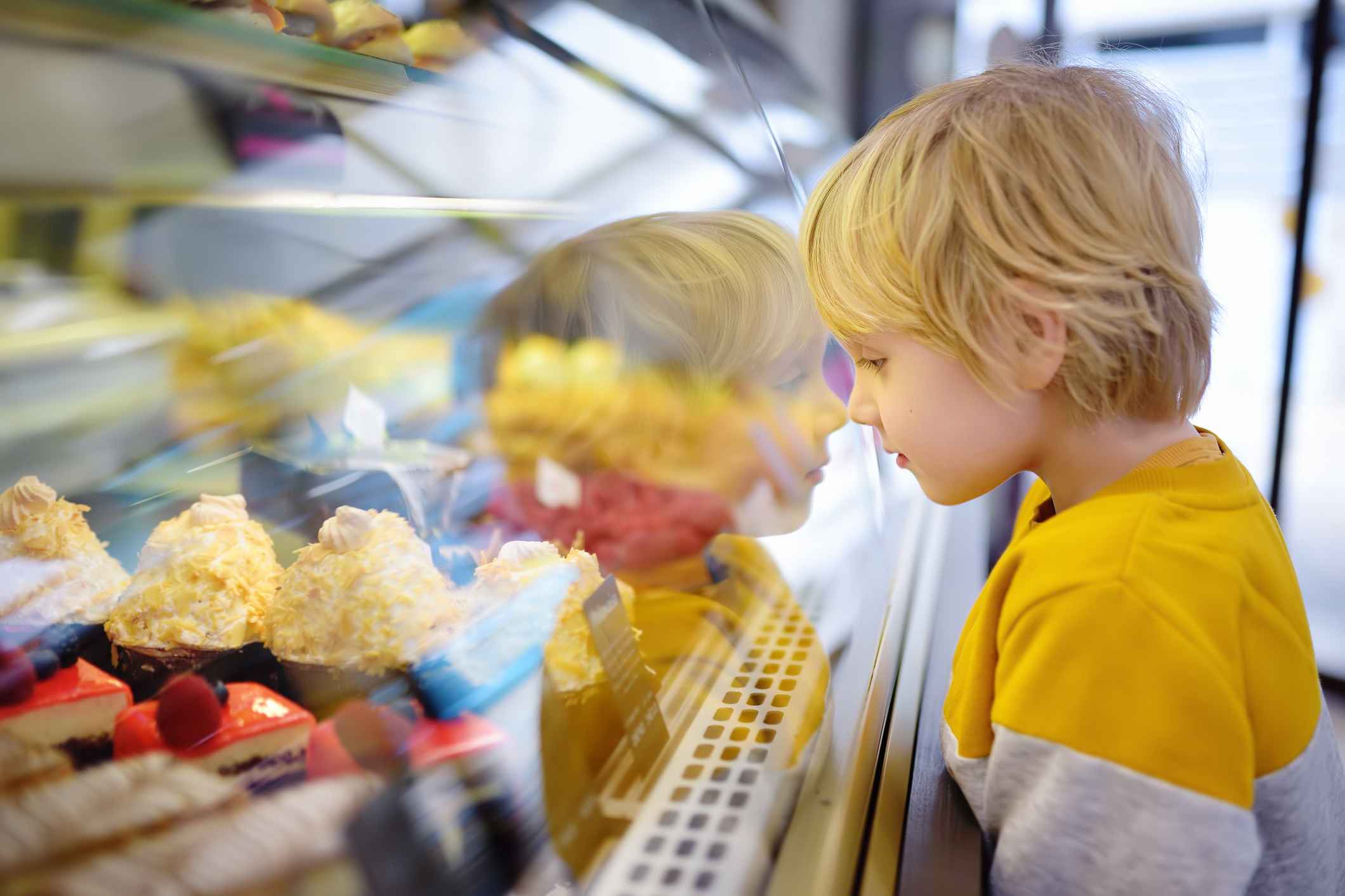 Little boy with food allergies is admiring cakes and other sweets on the showcase in cafe or supermarket.