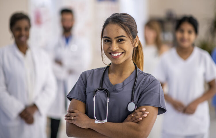 A diverse group of doctors are indoors in a medical clinic. They are standing in a group and smiling for the camera.