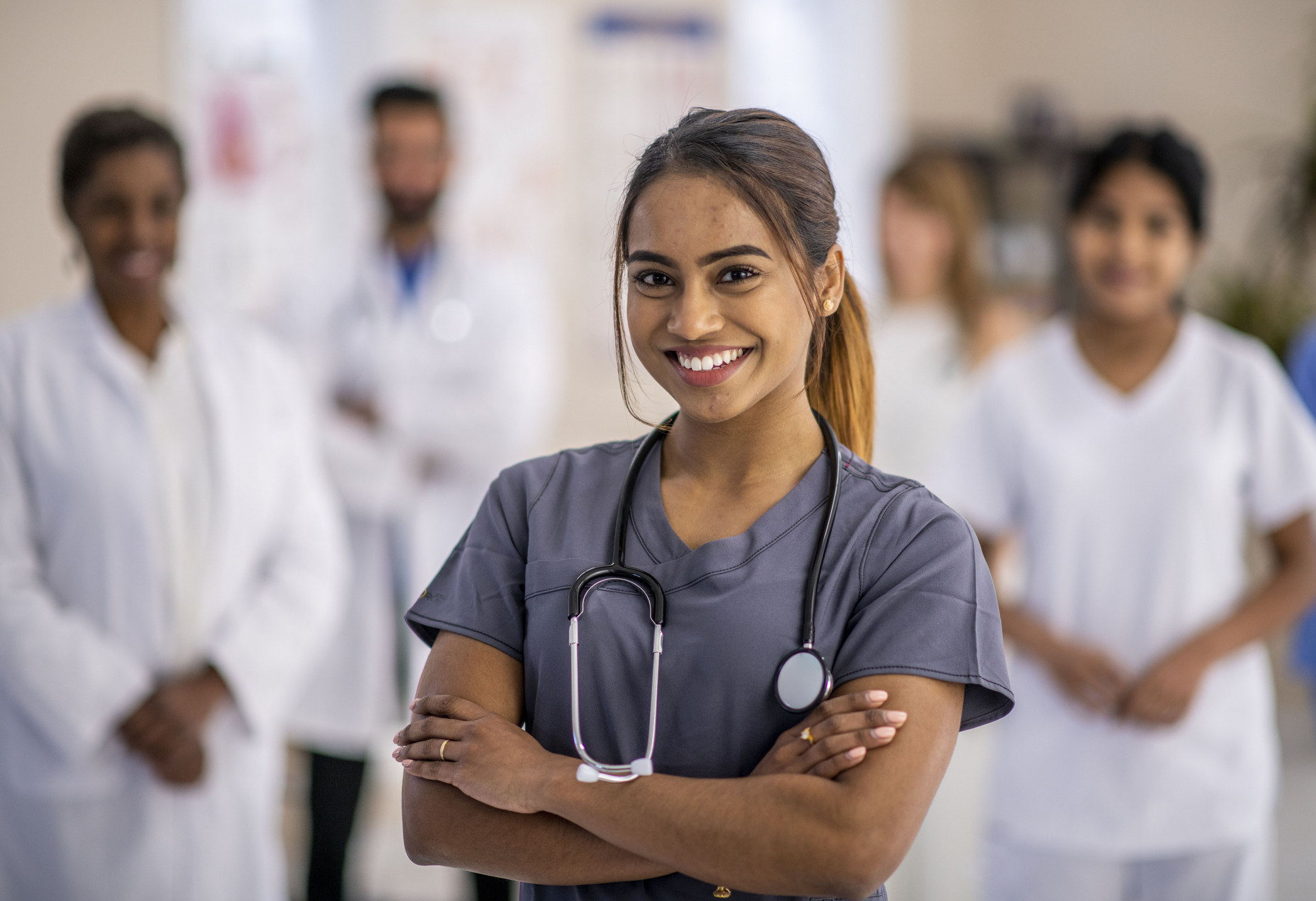 A diverse group of doctors are indoors in a medical clinic. They are standing in a group and smiling for the camera.