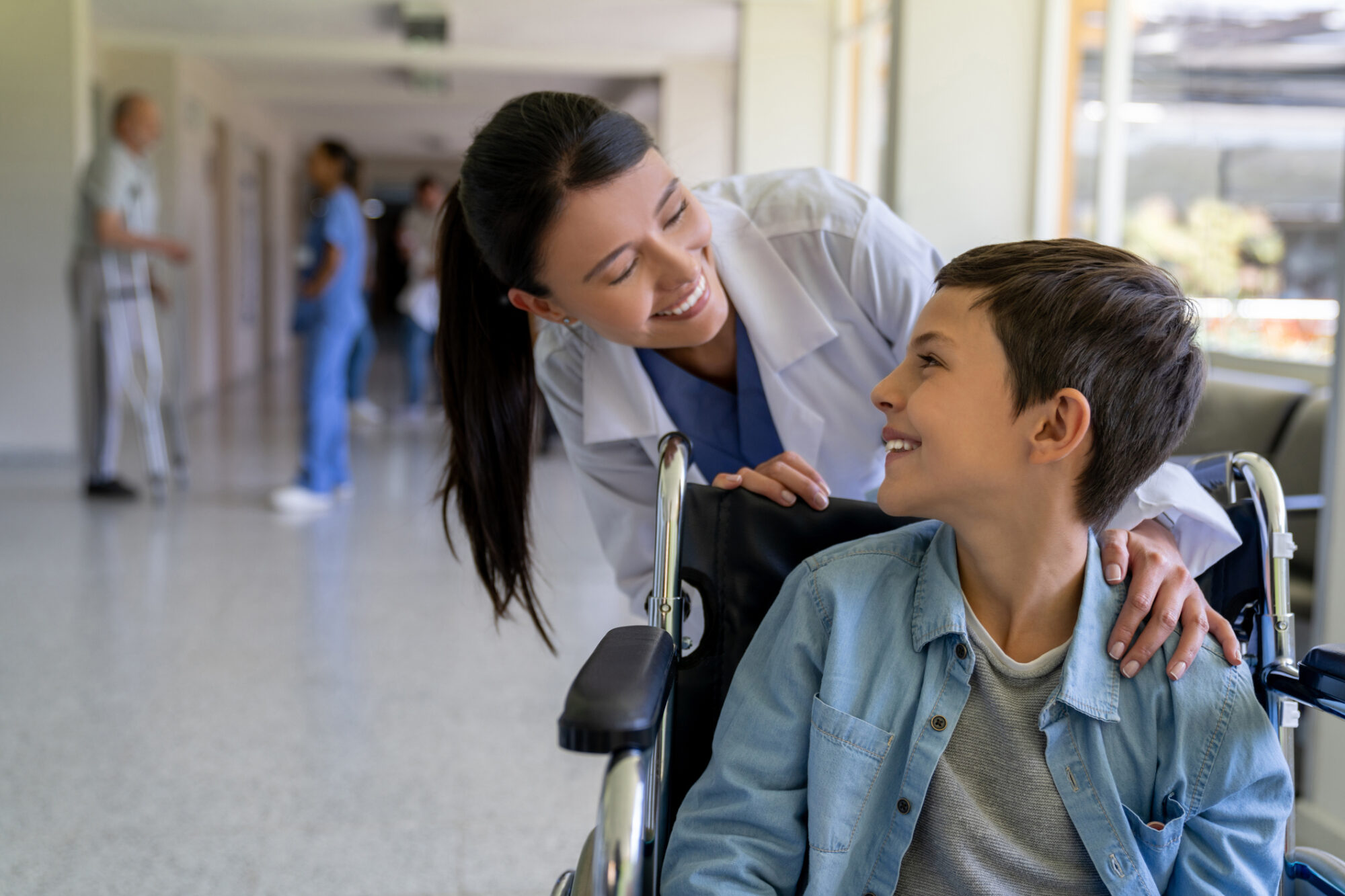 Resident doctor greeting a young patient in a wheelchair at the hospital and smiling