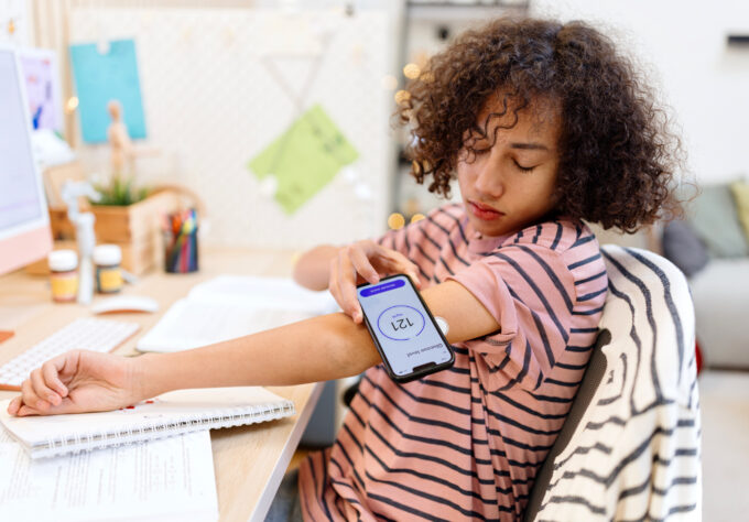 Teenager with type 1 diabetes using an app to check his sugar level at home while working on homework