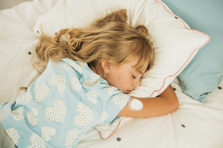 Young girl with glucose meter on her arm laying on bed and sleeping.