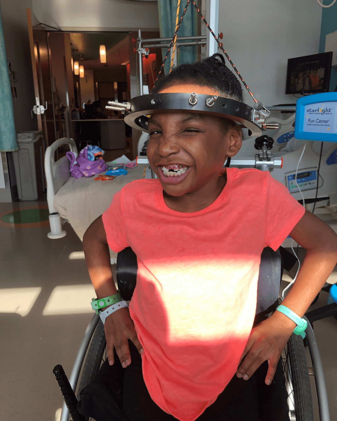 Girl with halo and wearing an orange shirt smiling in a hospital room.