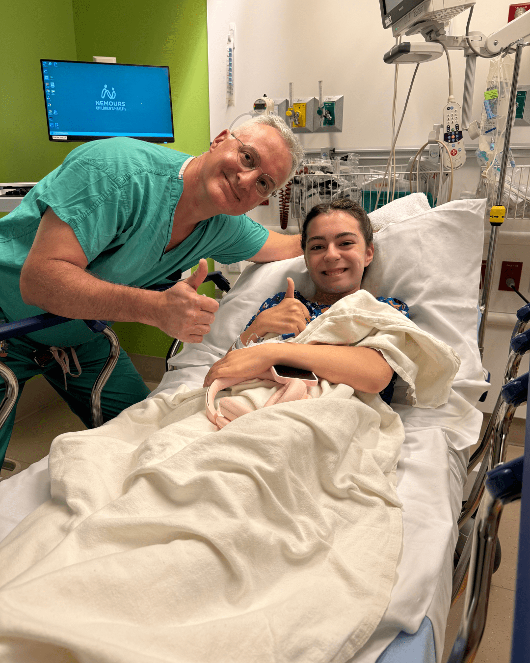 Teen girl and her orthopedic surgeon smile and give a thumbs up for a photo prior to surgery.