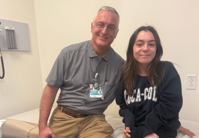 Teen girl and her orthopedic surgeon smile together for a photo in a hospital clinic room.