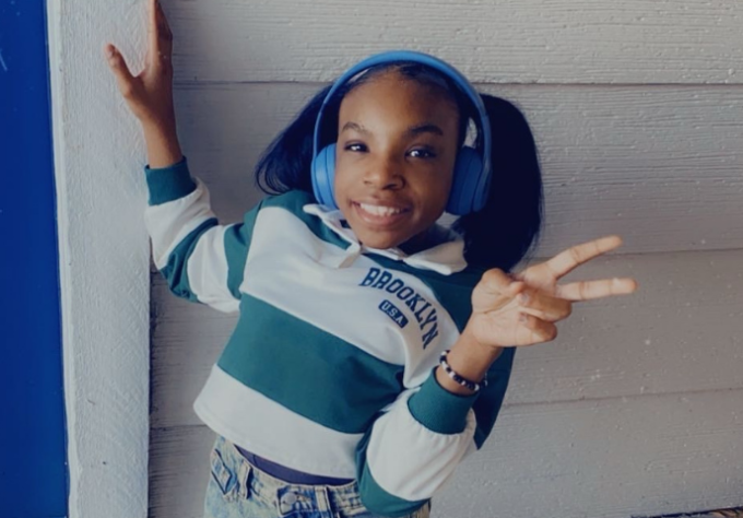 Girl with striped shirt and blue headphones poses in front of a white wall.