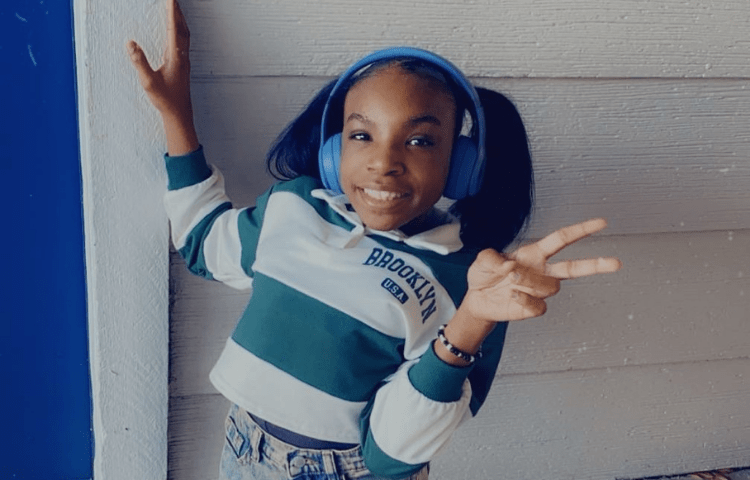 Girl with striped shirt and blue headphones poses in front of a white wall.