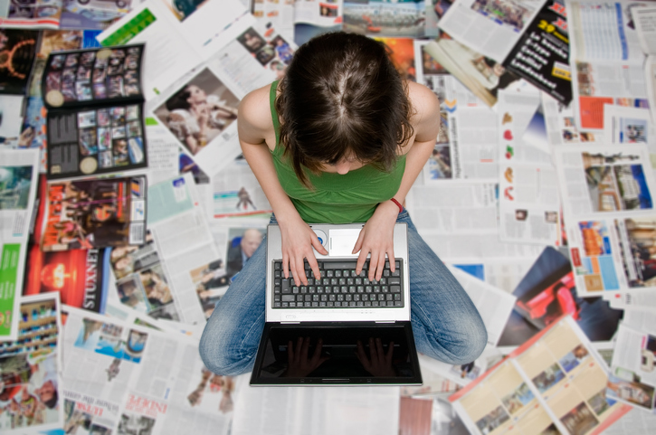 Young girl with a laptop sitting on newspapers representing the importance of setting limits to news exposure.