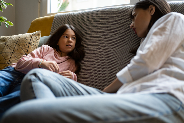 Mother and daughter sitting on the sofa while having a casual conversation about news and current events.