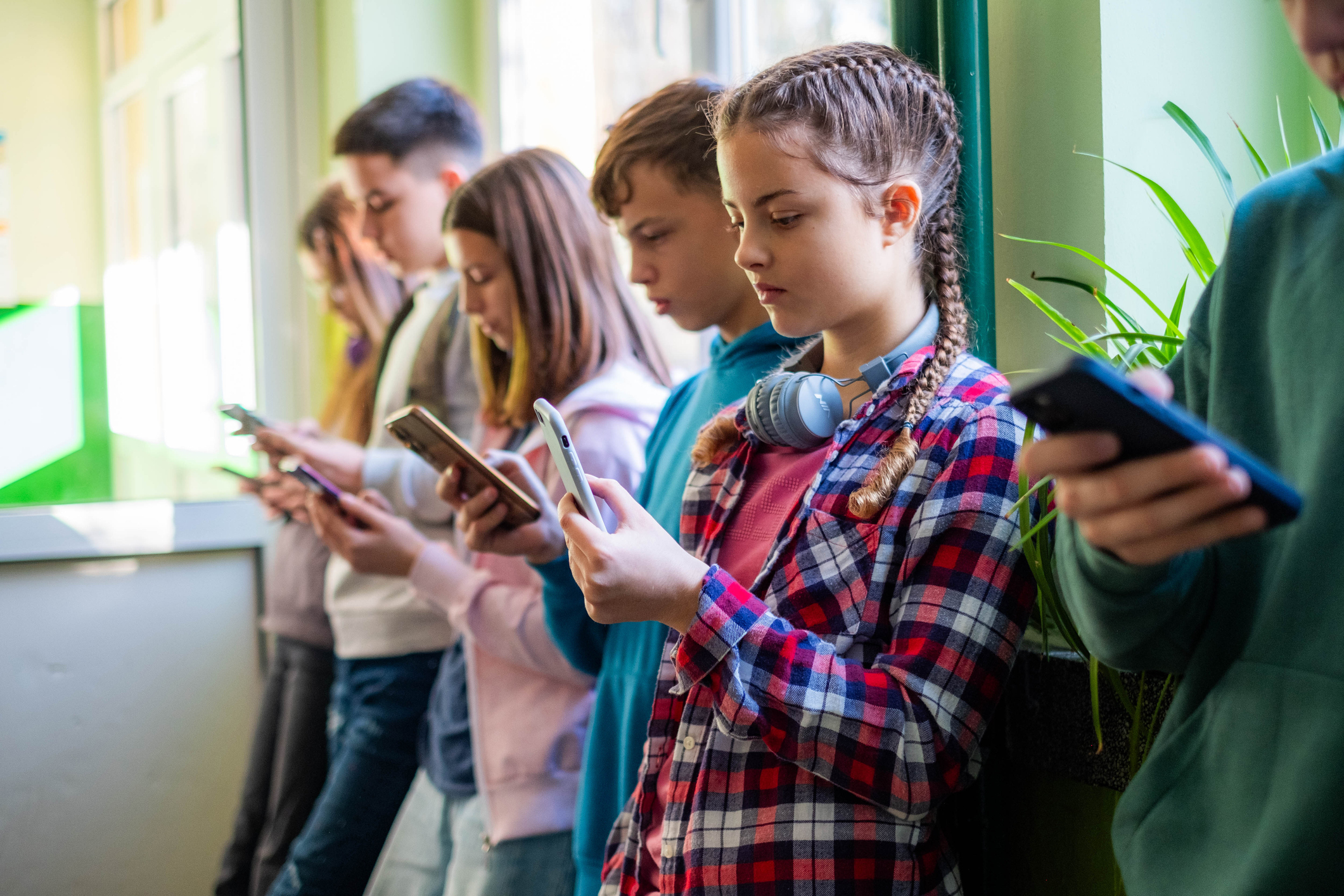 Teenage students are standing in the school hallway, all looking at news and social media on their phones.