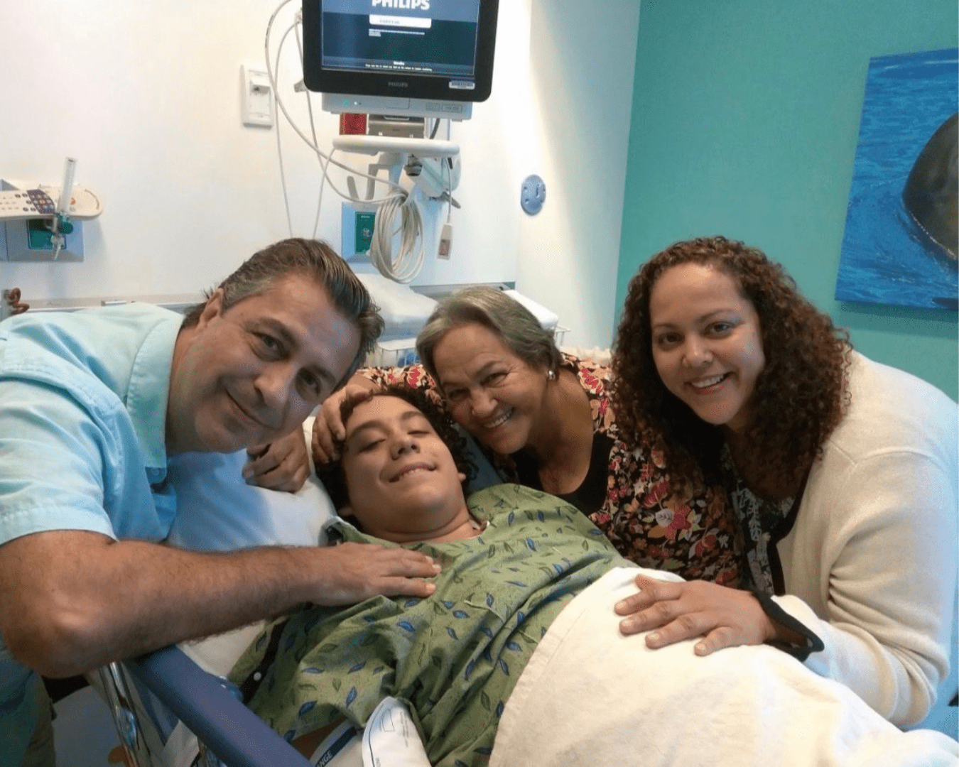 Teen male in hospital bed smiles for photo with family members before going into surgery