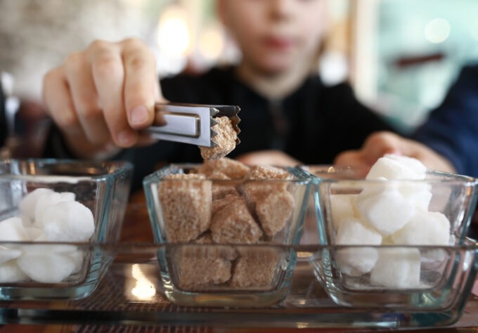 Child taking piece of sugar substitute with tongs in restaurant
