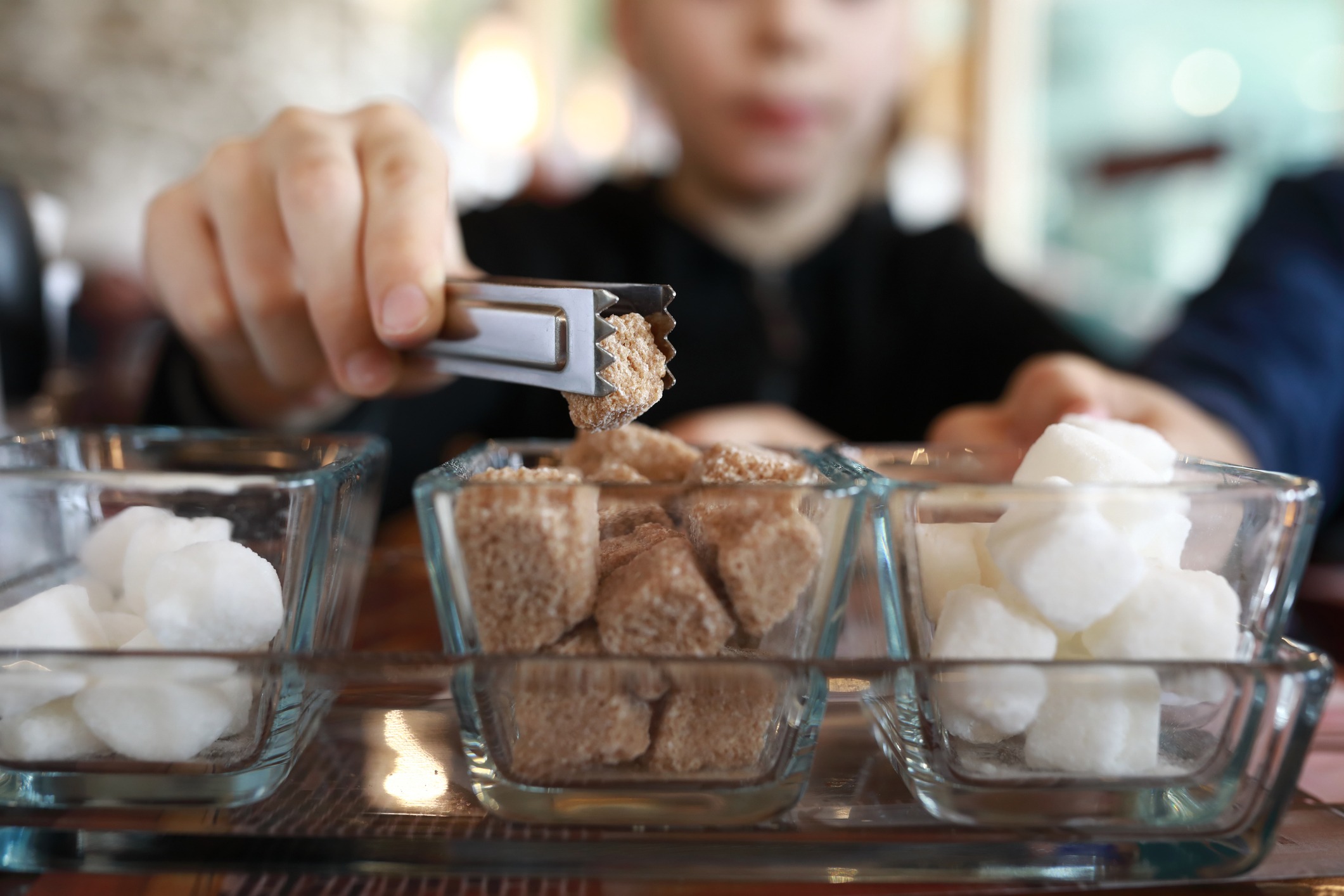 Child taking piece of sugar substitute with tongs in restaurant