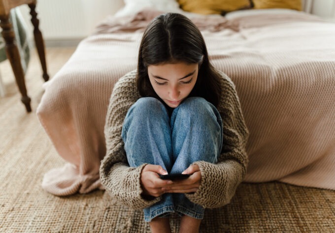 Teenage girl sitting on the floor and scrolling social media on a smartphone.