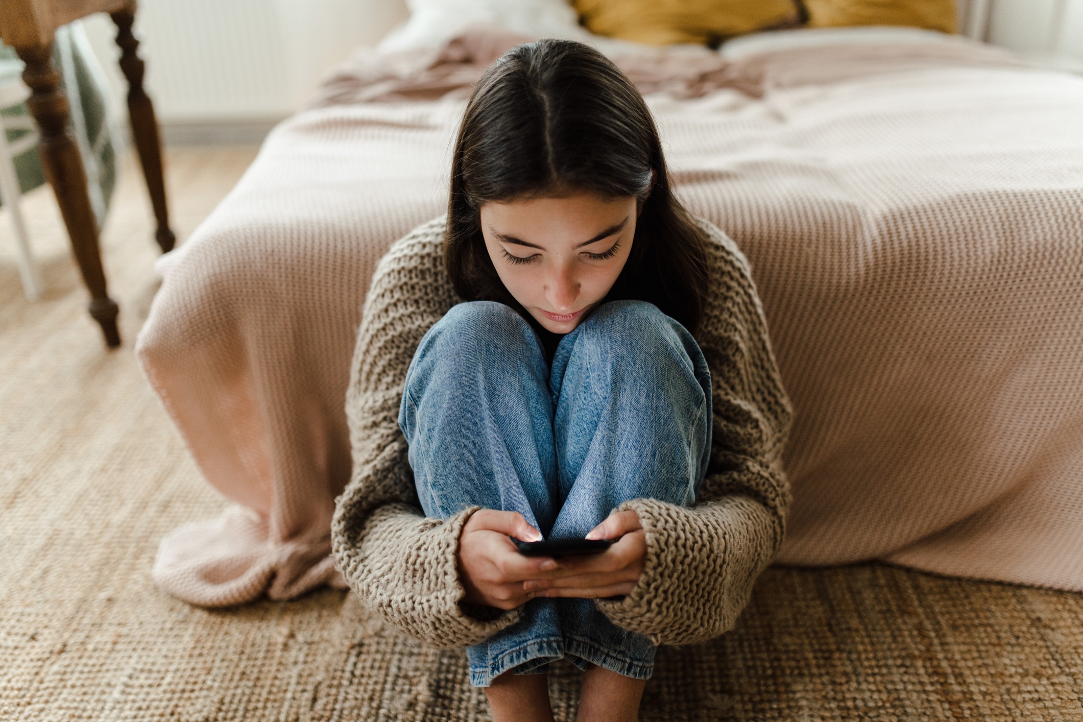 Teenage girl sitting on the floor and scrolling social media on a smartphone.