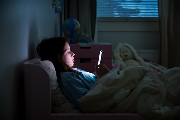 A child using smart phone while lying in bed late at night.