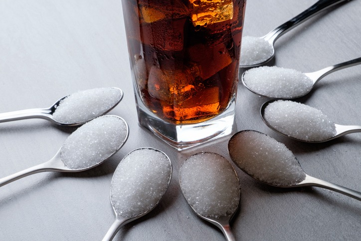 Close-Up Of Drink Amidst Sugar In 8 spoons On Table to represent how many teaspoons are in 10 ounces of soda