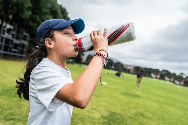Child girl drinking water on the sports field to stay hydrated