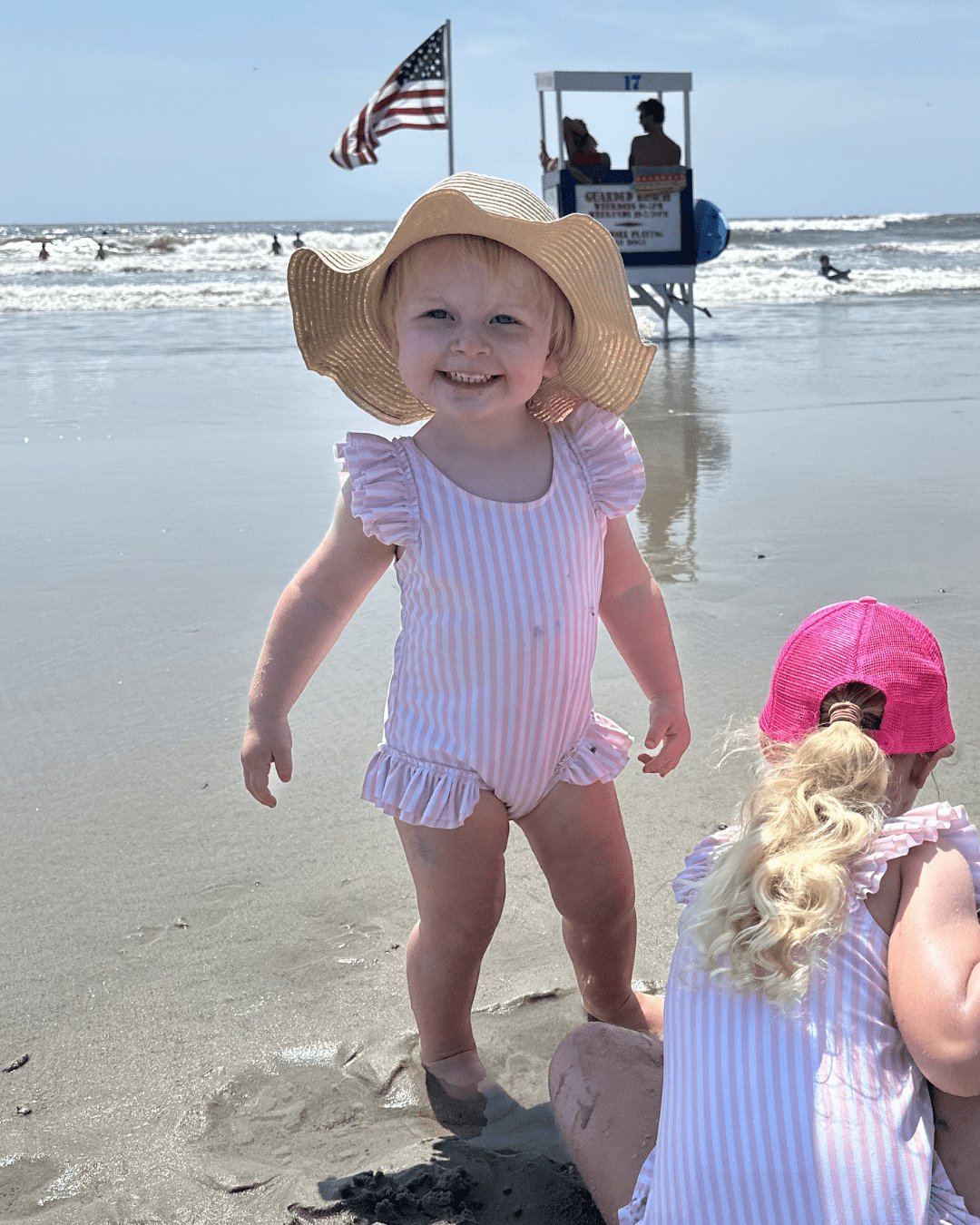 Young girl in pink and white striped swimming suit with a straw sunhat smiles on the beach for a photo