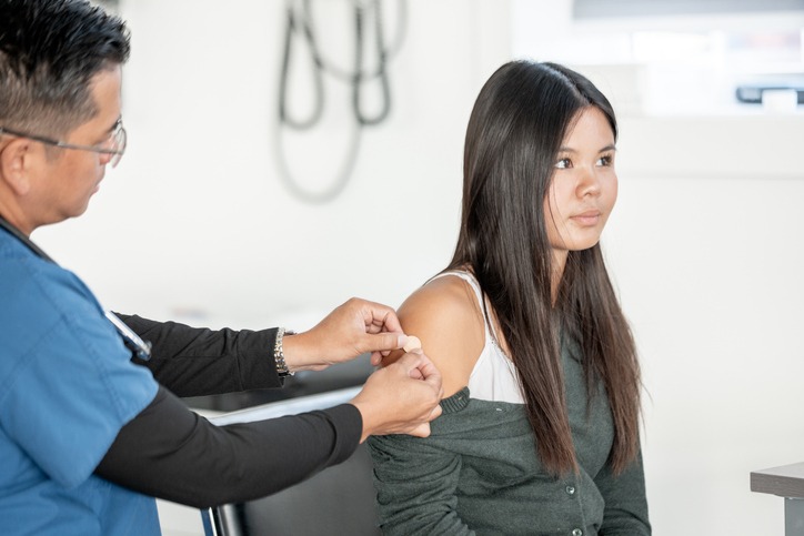 A compassionate doctor administers an HPV vaccine to a seated young woman in a bright clinical setting, conveying care, trust, and professional healthcare.