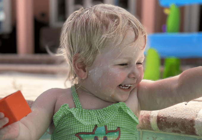 Blonde child in green swimsuit smiles while playing in the pool