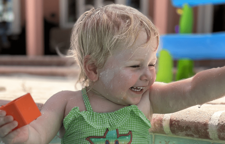 Blonde child in green swimsuit smiles while playing in the pool