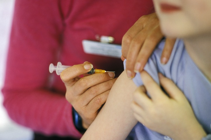 A child about to be given the MMR (mumps, measles, rubella) vaccination into their arm by a surgery nurse with a hypodermic syringe.