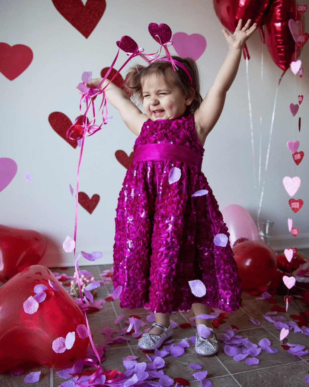 Toddler girl in sparkly pink dress throws heart-shaped confetti for a Valentines-themed photo shoot