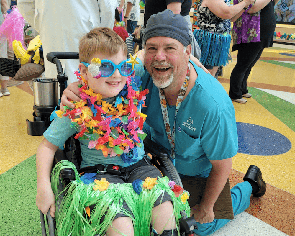 Boy in wheelchair smiles for photo with physician at luau-themed hospital event